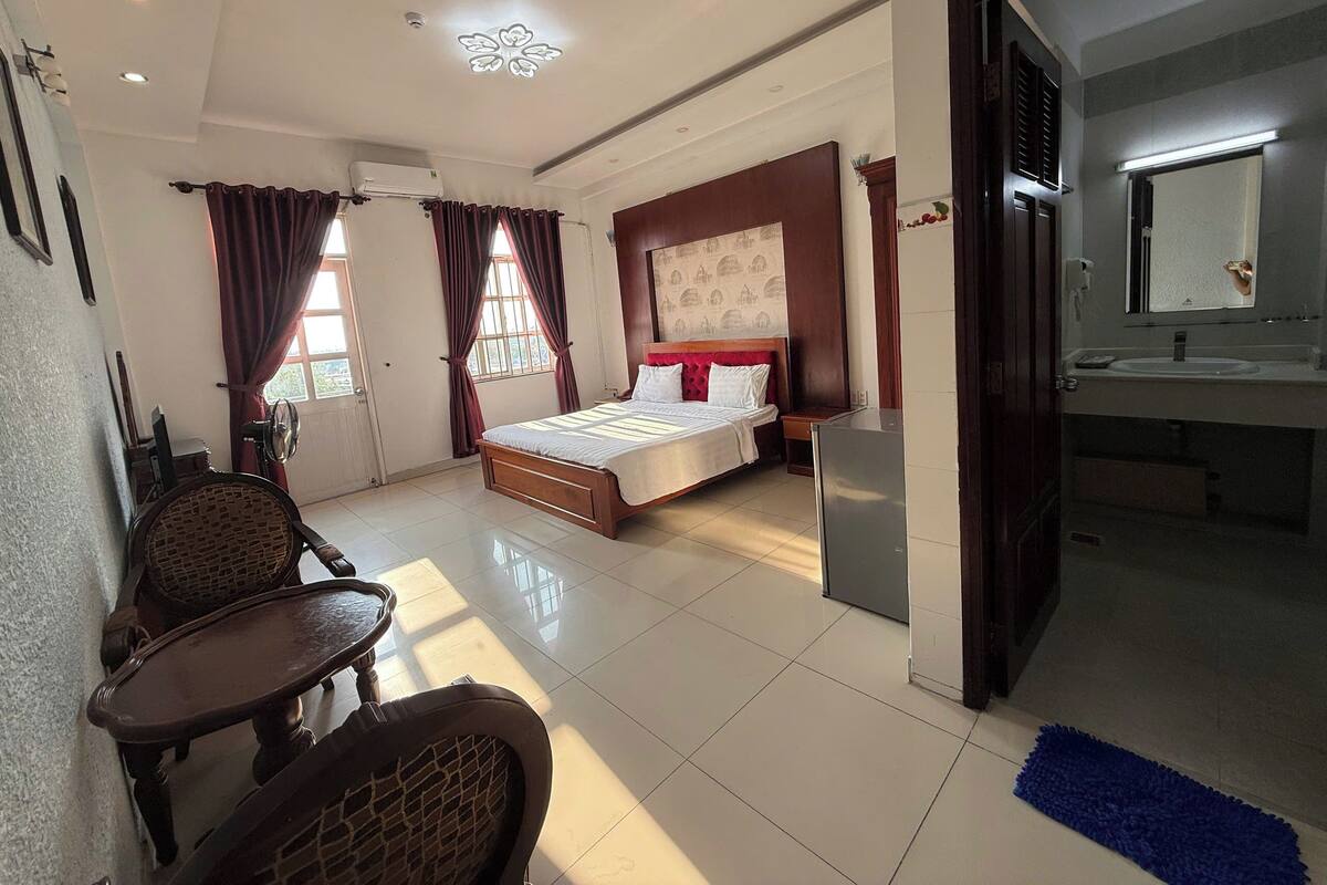 A hotel room with a bed, bedside table, chair, and a bathroom with a sink and mirror.