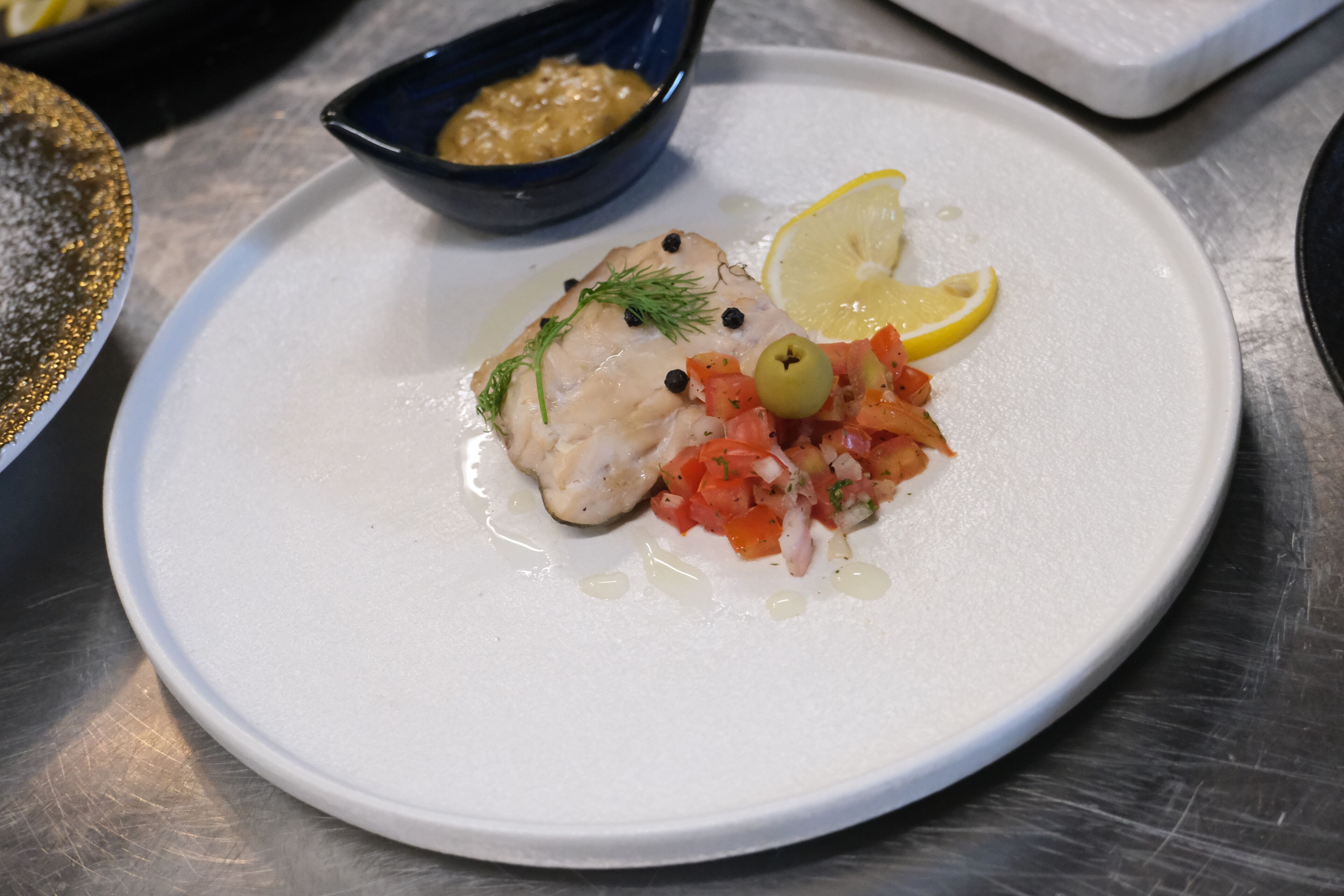 A plate with fish, a lemon wedge, and a small bowl of sauce.