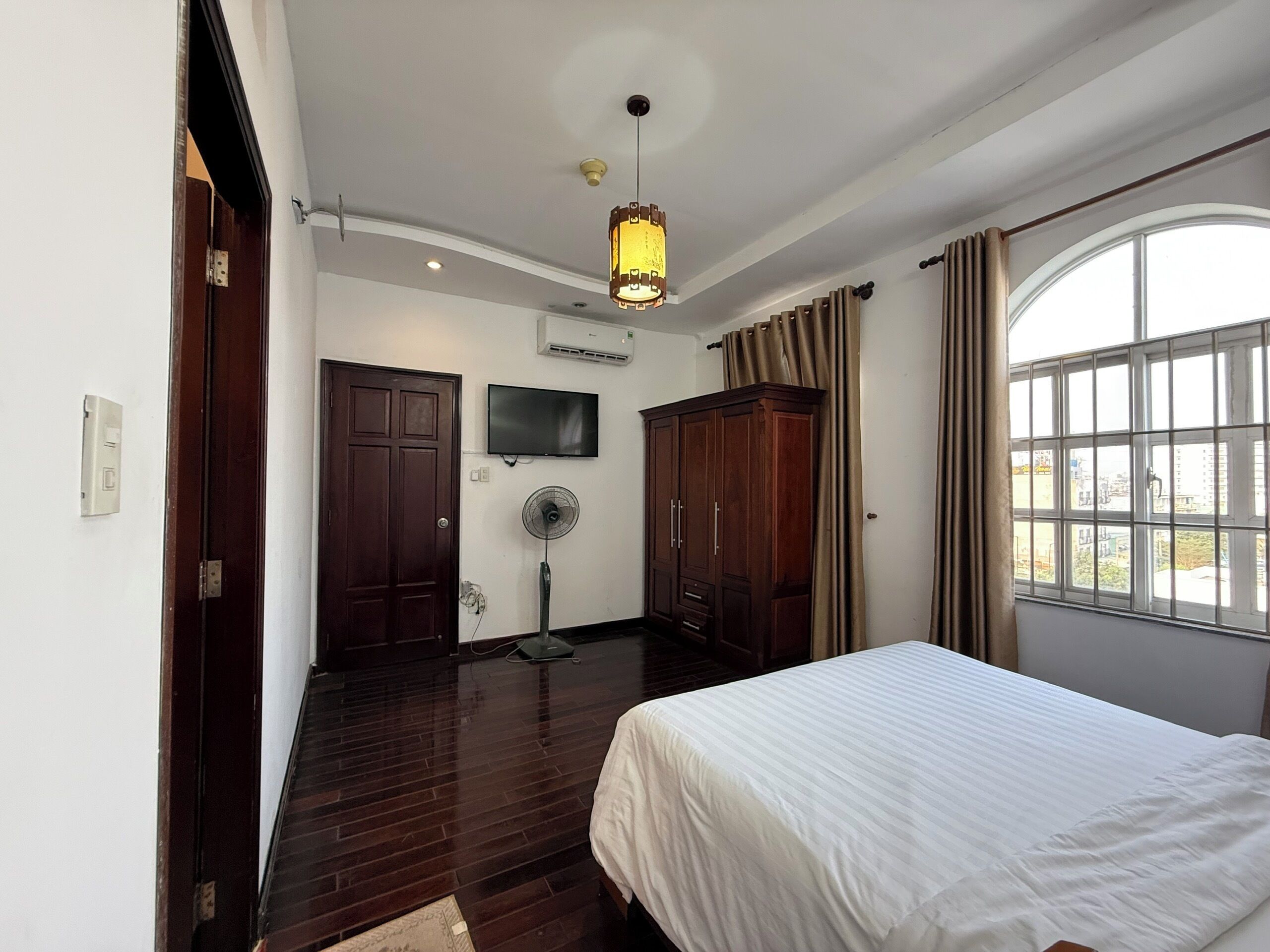 A bedroom with a bed, a ceiling fan, a TV, and a window with curtains.