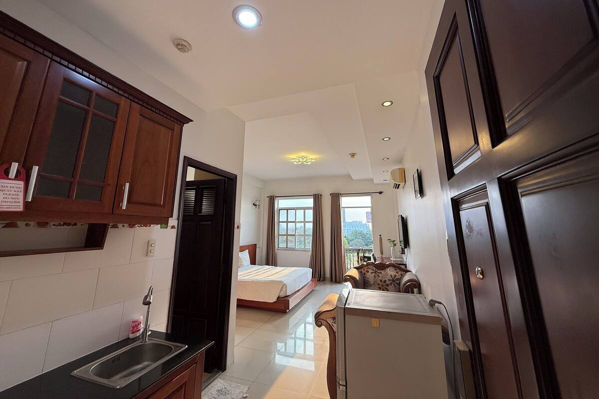 A compact hotel room with a kitchenette, a bed, a sofa, and a view of the cityscape.