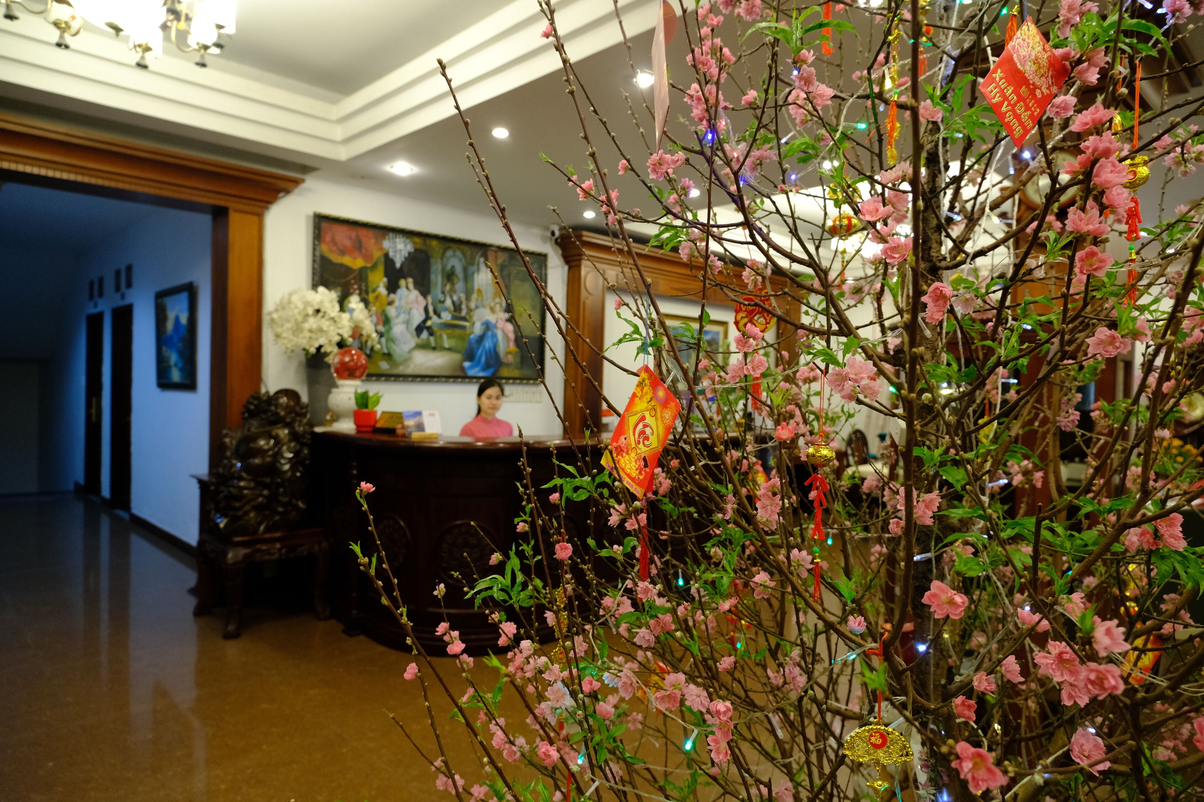 Un hall d’entrée avec un comptoir de réception, un tableau et un arbre décoratif orné de fleurs roses.