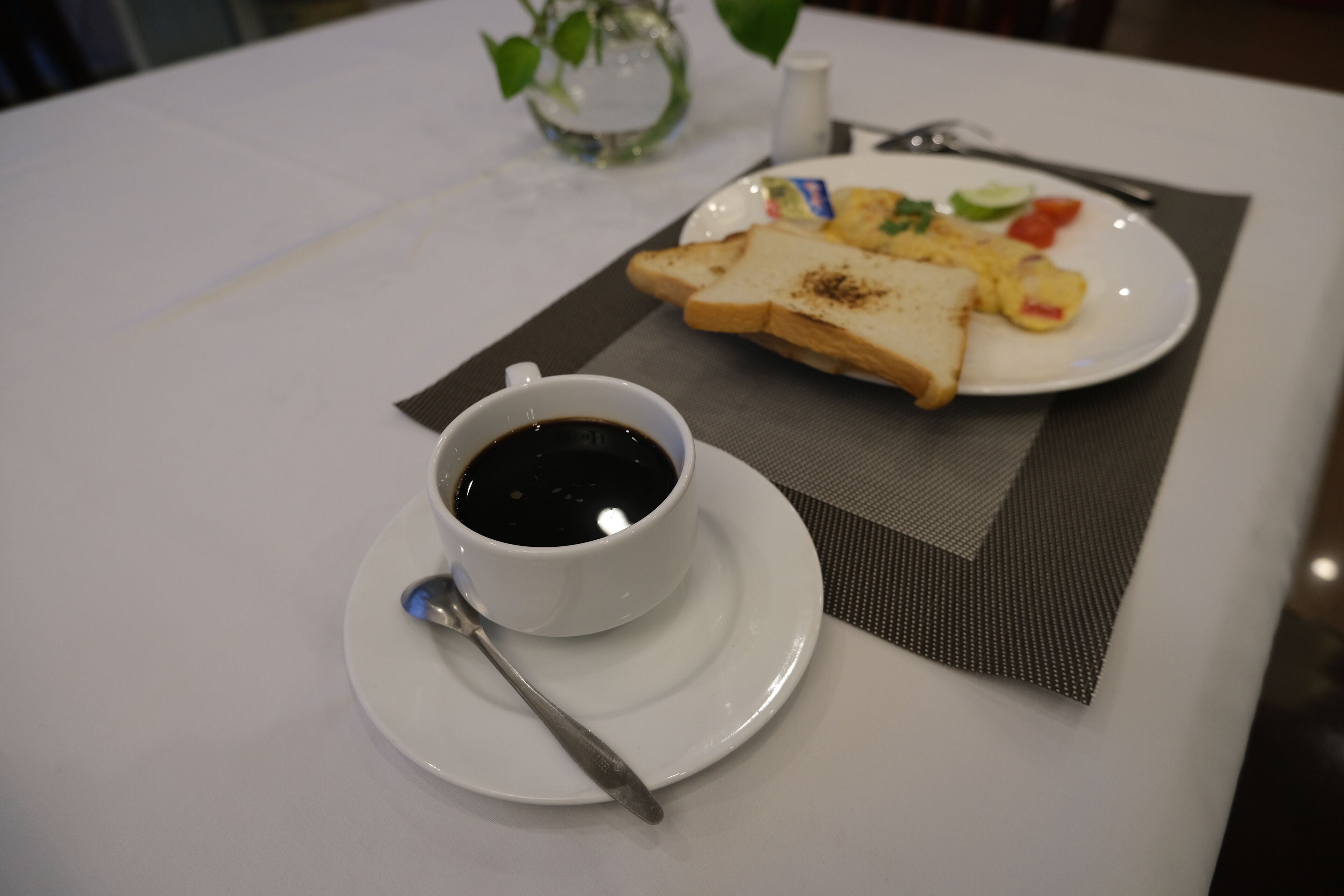 A breakfast table with a cup of coffee, toast, scrambled eggs, and a small plate of vegetables.