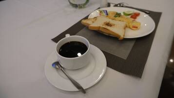 A breakfast table with a cup of coffee, toast, scrambled eggs, and a small plate of vegetables.