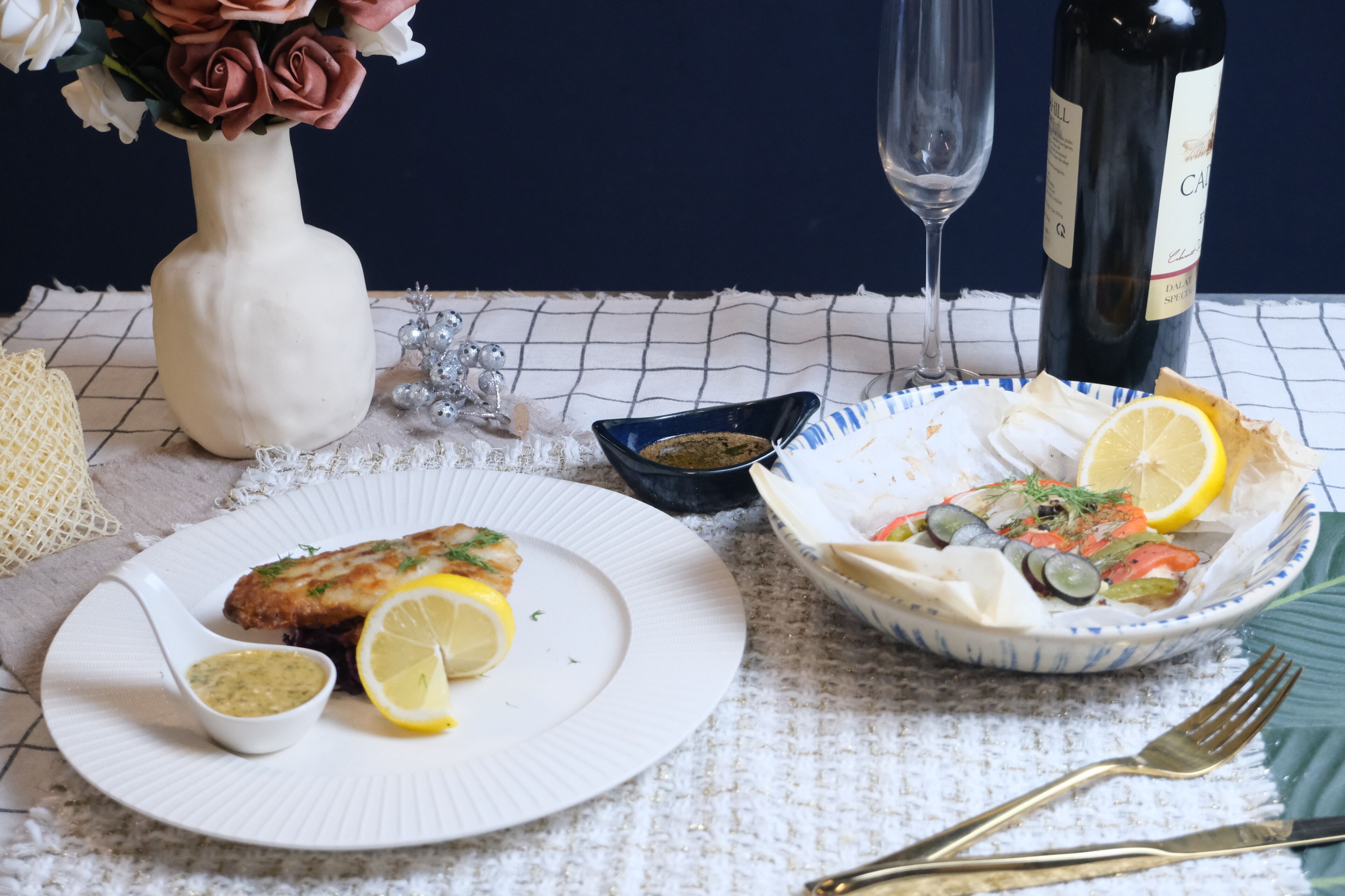A dining table with a plate of food, a bottle of wine, and a vase of flowers.