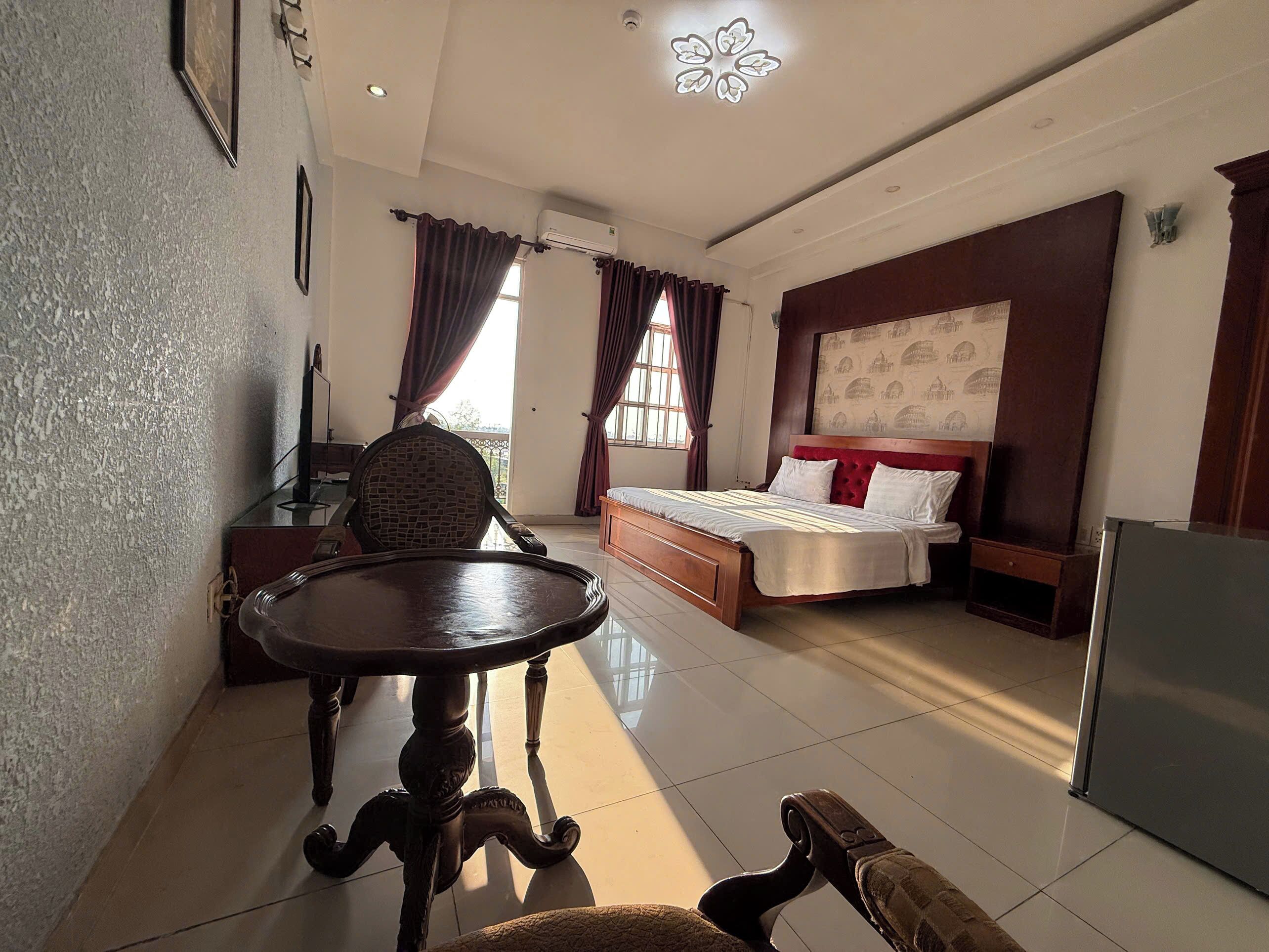 A hotel room with a bed, a desk, a chair, a table, and a refrigerator.