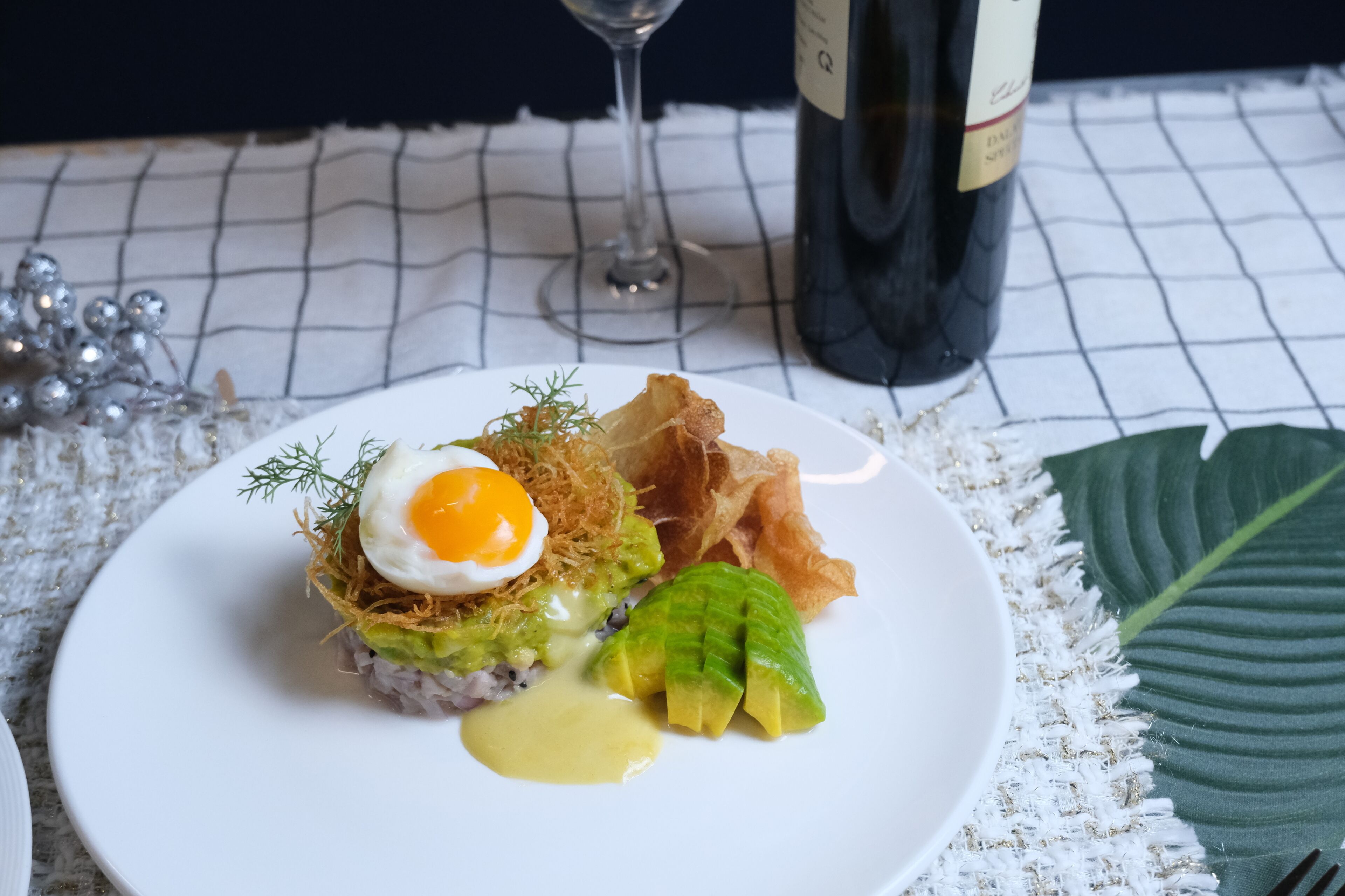 Un plato de comida con una botella y una copa de vino al fondo.
