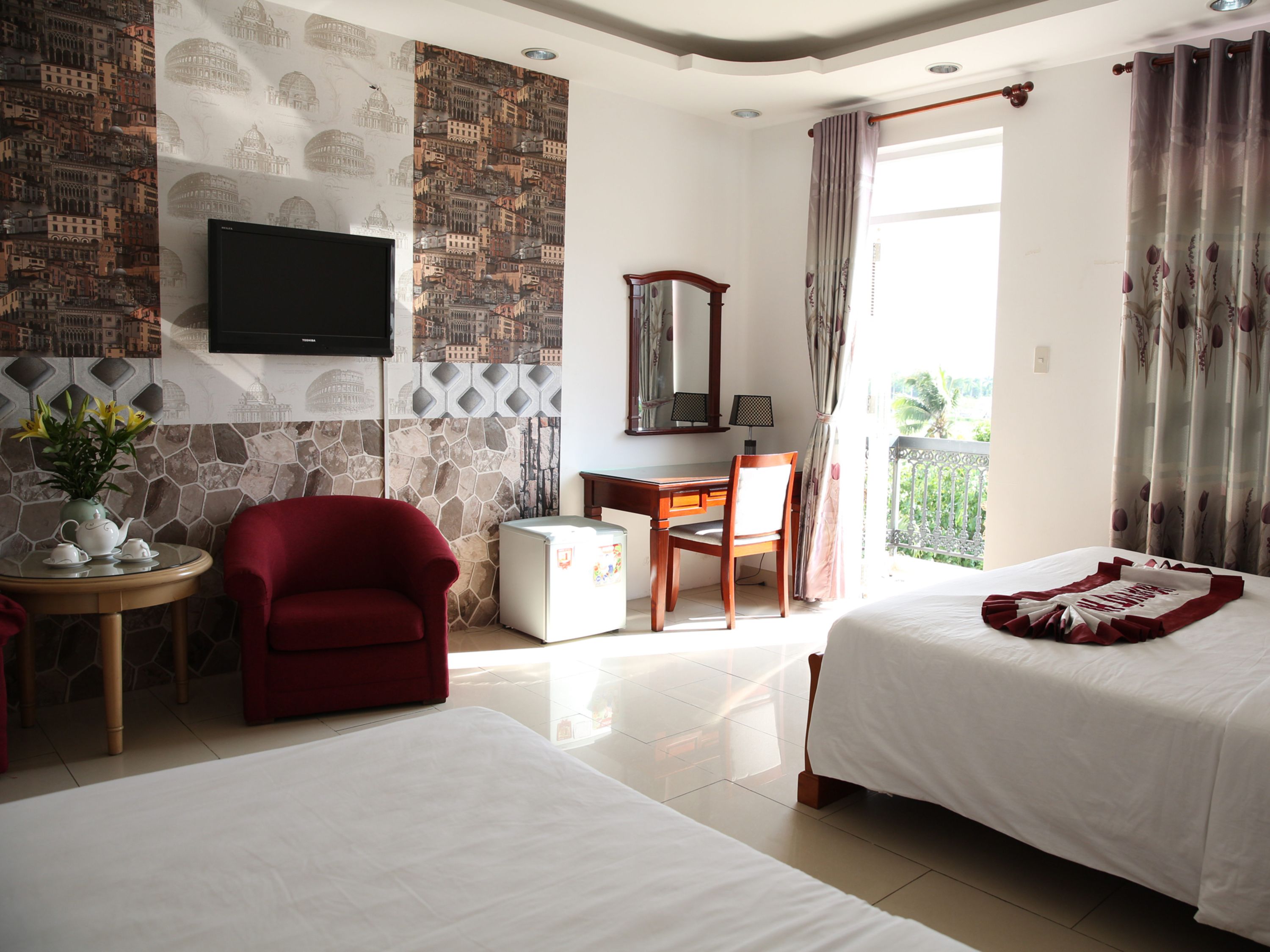 Habitación de hotel con dos camas, un escritorio, una silla, un televisor y un balcón con cortinas.