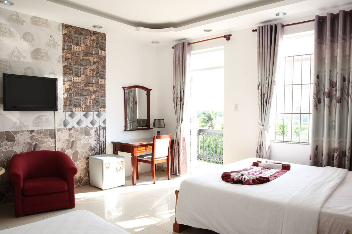 A hotel room with a bed, a desk, a chair, a TV, and a balcony with a view.