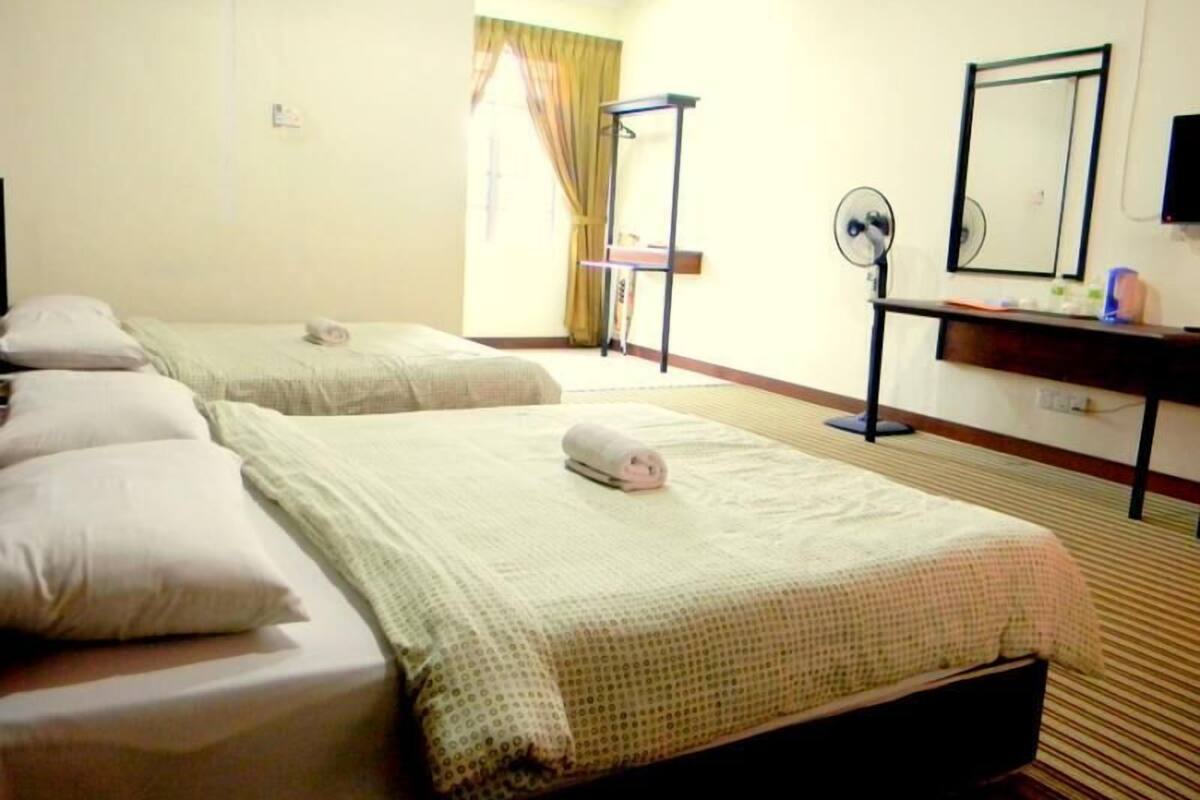 A hotel room with two beds, a desk with a mirror, and a standing fan.