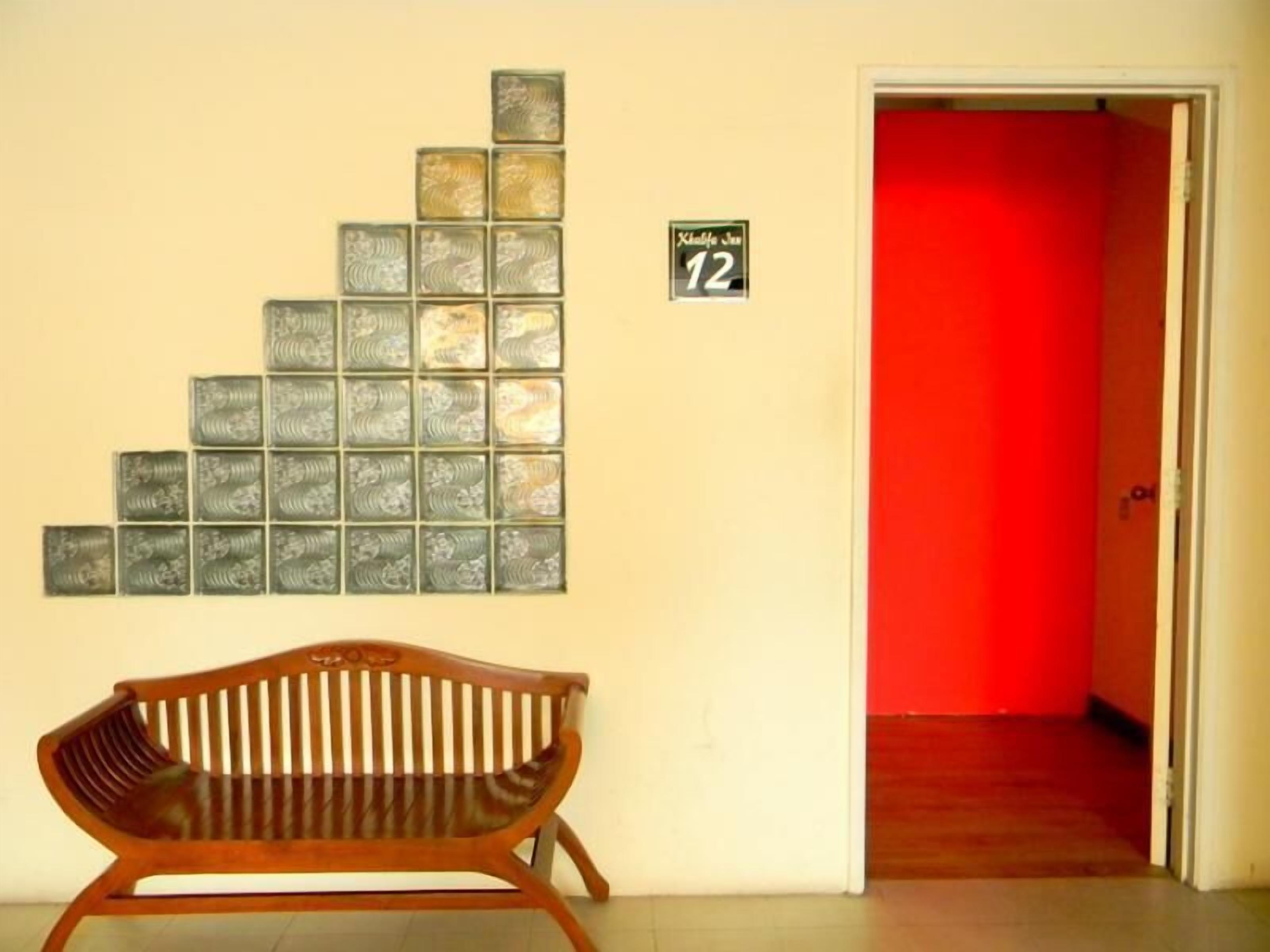 Een kamer met een houten bankje, een muur met een geometrisch patroon en een rode deur.