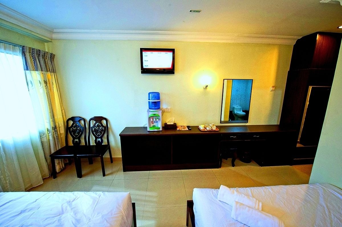 A hotel room with two beds, a desk with a computer monitor, a water dispenser, and a mirror.