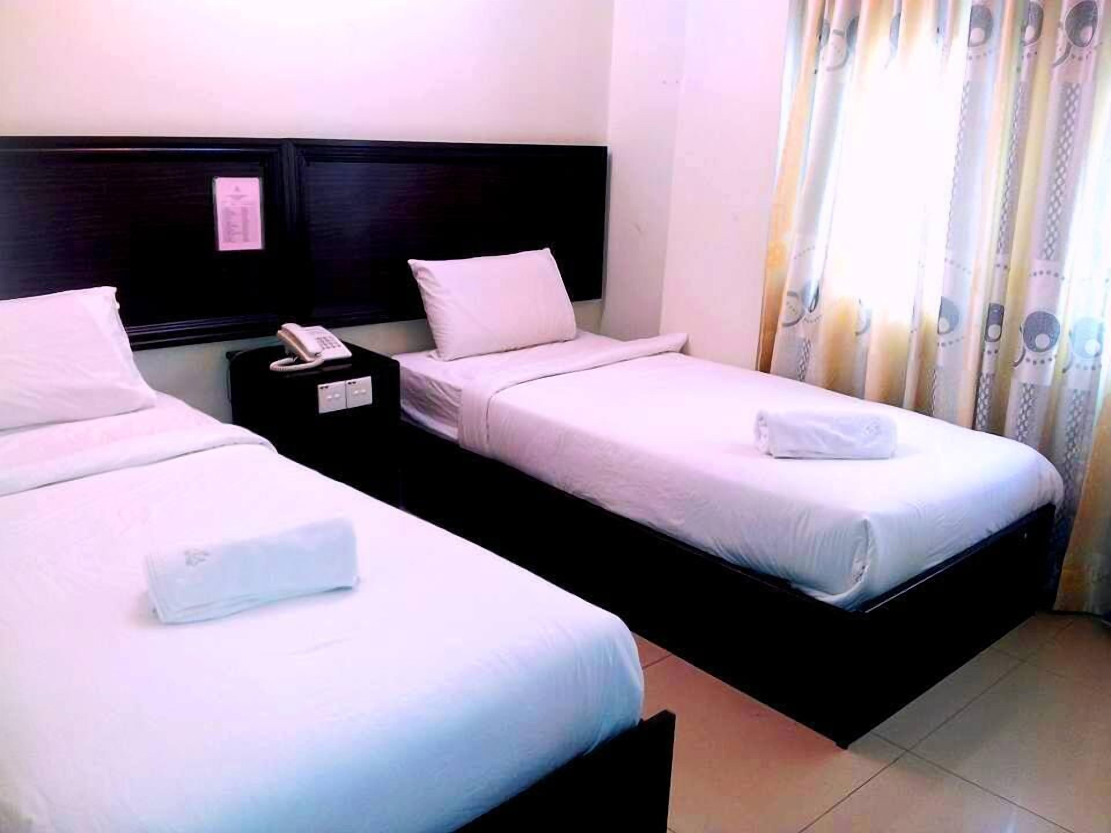 Habitació d'hotel amb dos llits individuals, una taula de nit amb un telèfon i una finestra amb cortines.