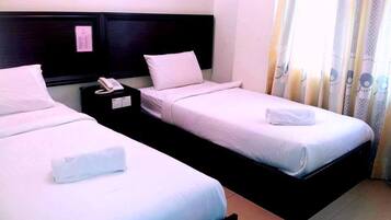 Habitació d'hotel amb dos llits individuals, una taula de nit amb un telèfon i una finestra amb cortines.