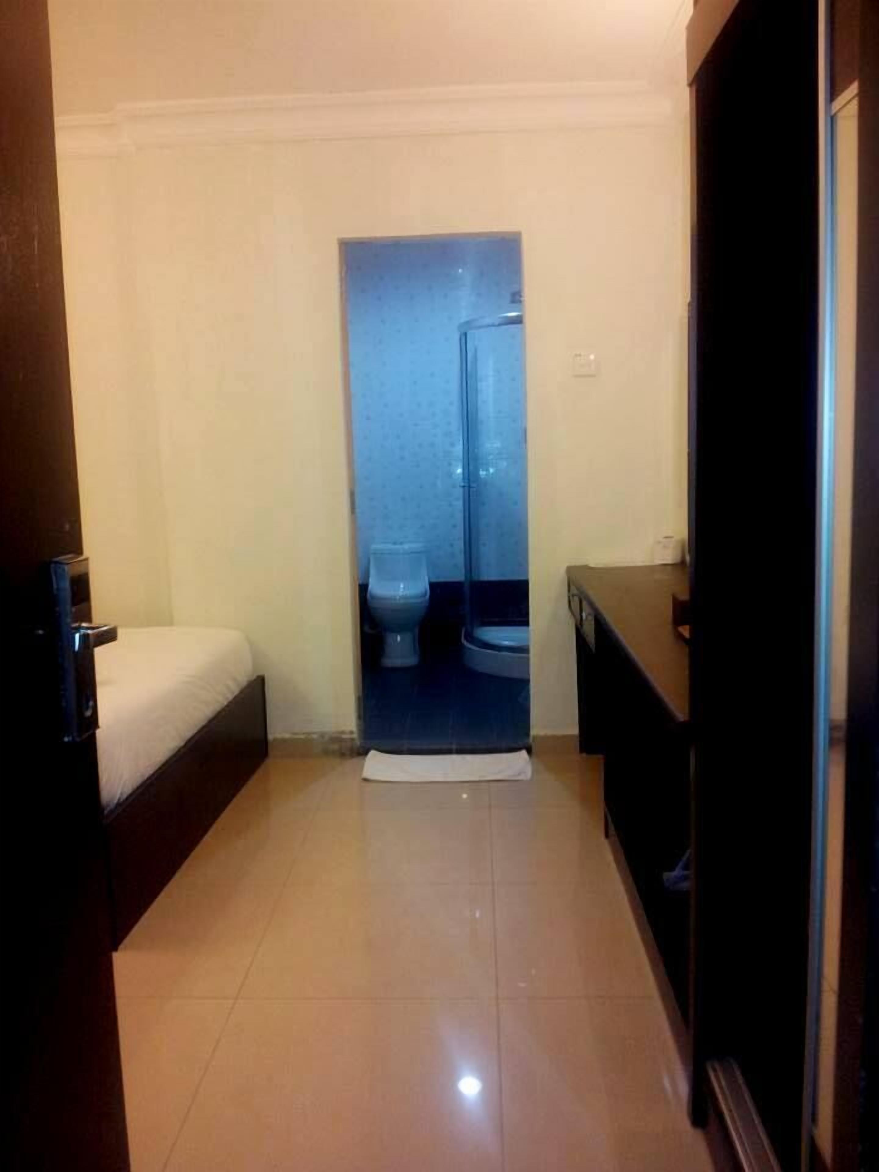 Una camera d'albergo piccola e stretta, con un letto, un water e un lavandino.
