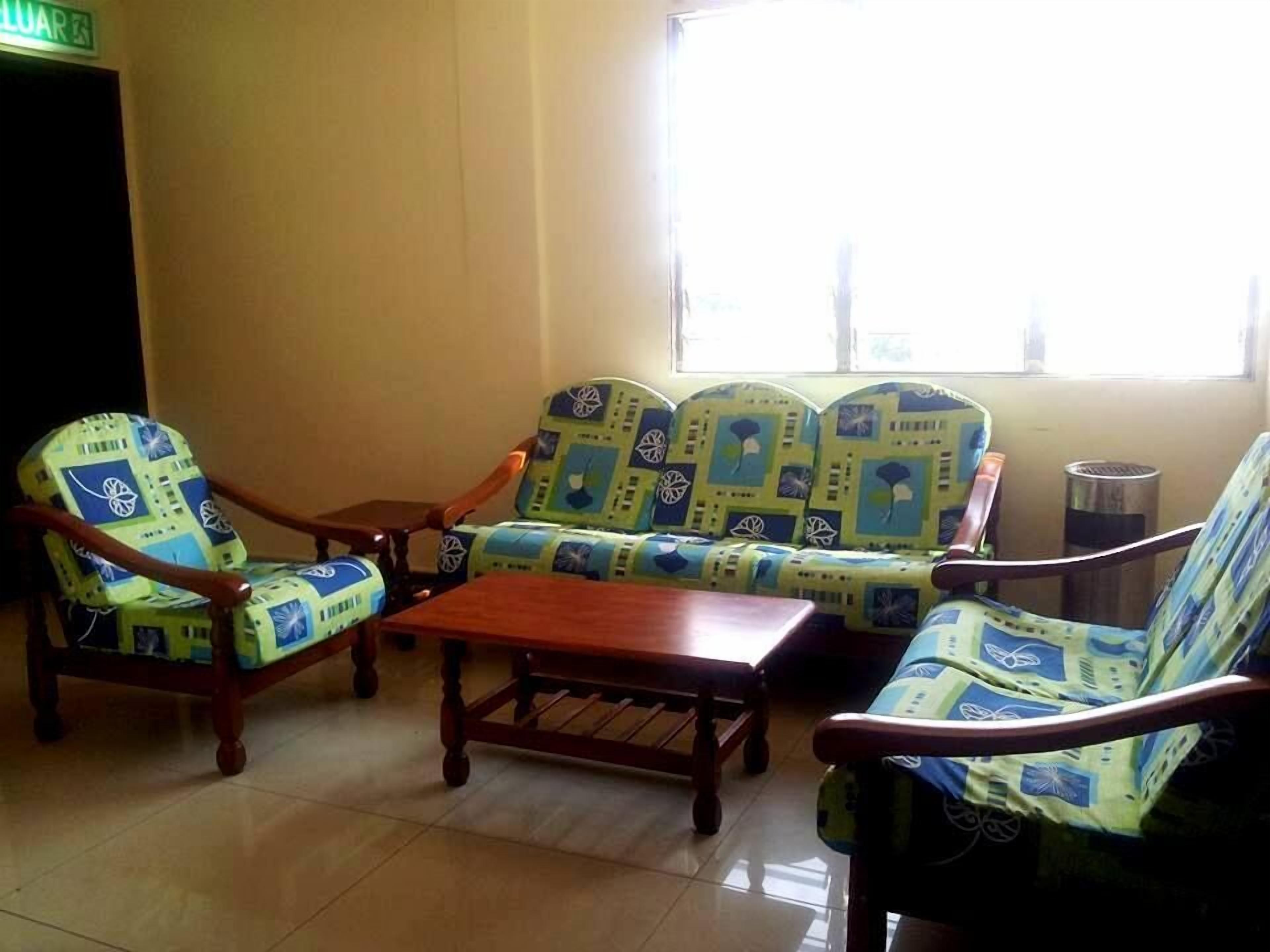 Un espacio de descanso con sofás y sillones estampados, una mesa de centro de madera y piso de baldosas.
