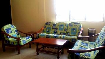 Un espacio de descanso con sofás y sillones estampados, una mesa de centro de madera y piso de baldosas.