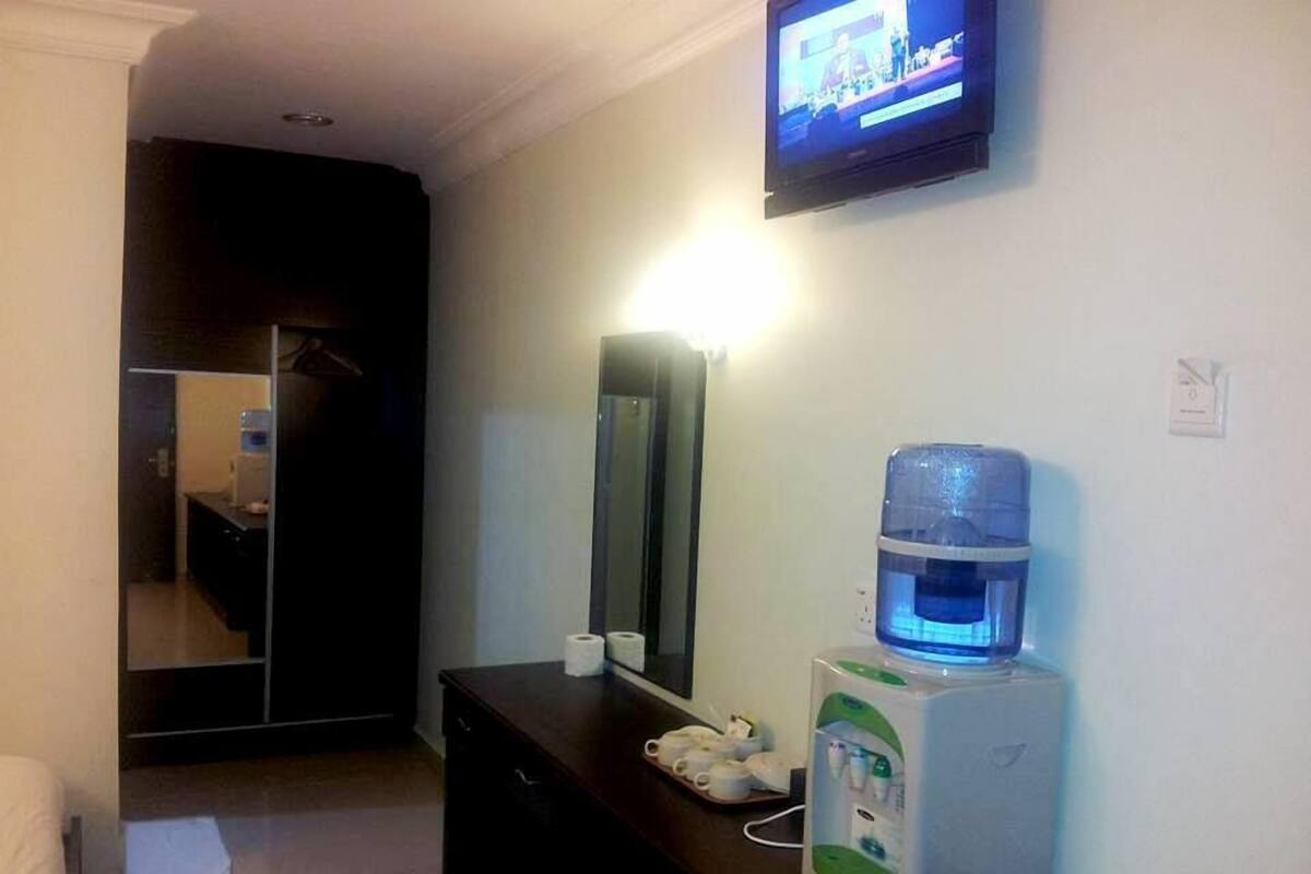 Ein Hotelzimmer mit Bett, Nachttisch mit Wasserspender, Telefon und an der Wand montiertem Fernseher.