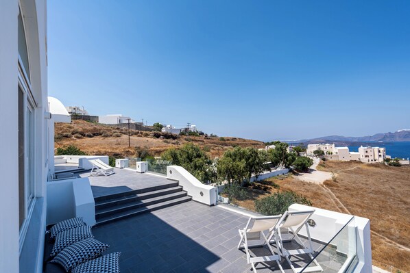 A modern building with a terrace, steps leading to a deck, and a view of the sea and hills. - The Zen Villa (Santorini)