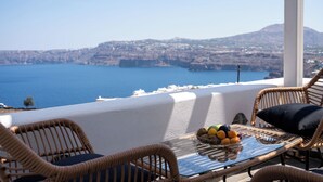 A balcony with wicker chairs and a table, overlooking a coastal landscape with a clear view of the sea and distant hills. - The Zen Villa (Santorini)