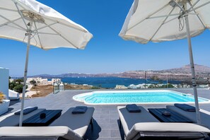 A poolside area with two sun loungers and white umbrellas, overlooking a clear blue sea and distant hills. - The Zen Villa (Santorini)