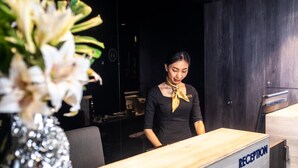 A reception desk with a sign reading "RECEPTION" and a woman standing behind it. - CUBE Family Boutique Capsule Hotel (Singapore)