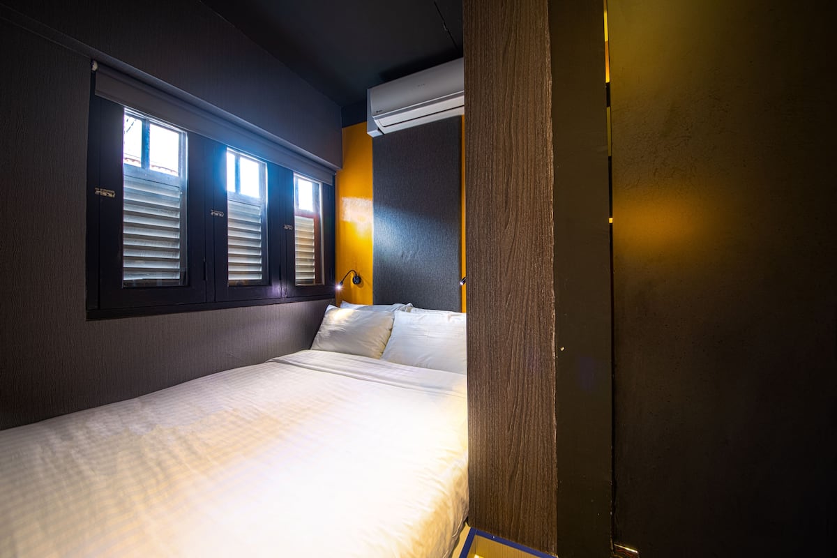 Ein Hotelzimmer mit Bett, Fenster mit Jalousien, Klimaanlage und Wandleuchte.