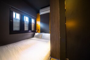 Une chambre d’hôtel comprenant un lit, une fenêtre avec des stores, un appareil de climatisation et un luminaire fixé au mur.