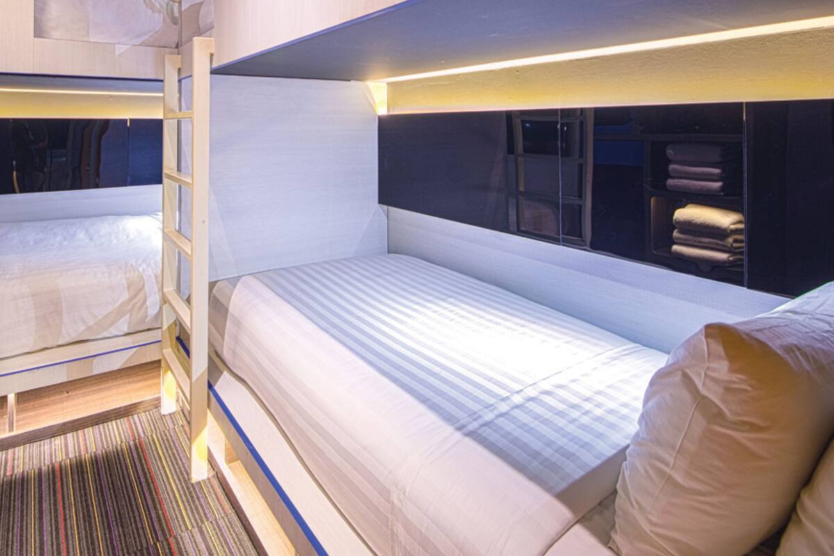 Ein modernes, kleines Hotelzimmer mit Stockbetten, einer kleinen Sitzecke und einem Fenster mit Vorhängen.
