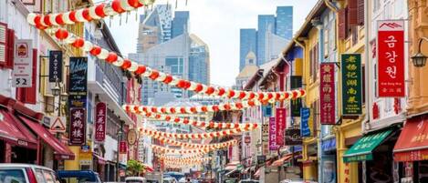 A street lined with shops and cars, with red and white lanterns hanging overhead.