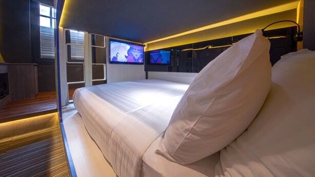 A modern hotel room with a large bed, a TV mounted on the wall, and a small seating area with a table and chairs. - CUBE Family Boutique Capsule Hotel (Singapore)