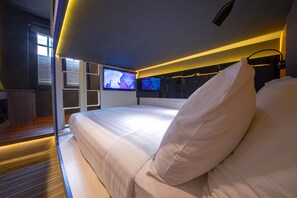 A modern hotel room with a large bed, a TV mounted on the wall, and a small seating area with a table and chairs. - CUBE Family Boutique Capsule Hotel (Singapore)