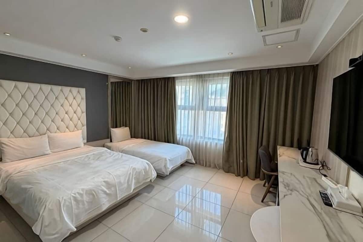 A hotel room with two beds, a desk, a chair, a TV, and a window with curtains.