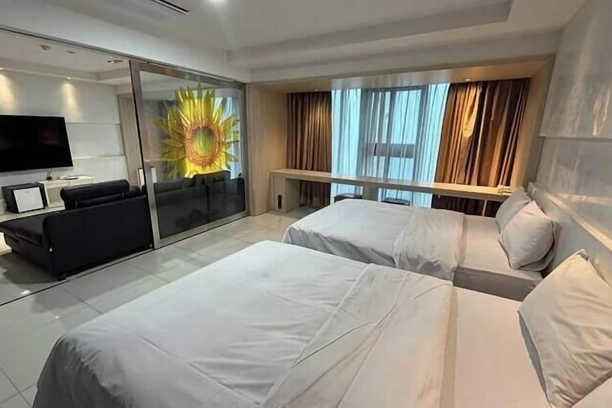 A hotel room with two beds, a sofa, a TV, and a large window with curtains.