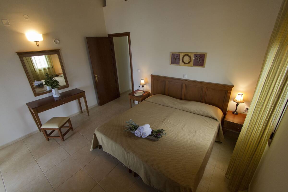 A bedroom with a bed, a desk, a chair, a mirror, and two bedside tables with lamps.