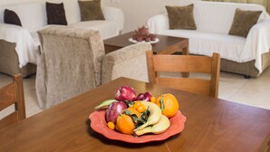 A dining area with a wooden table set with fruit, two sofas, and a window with curtains. - Secreto Studios (Kissamos)