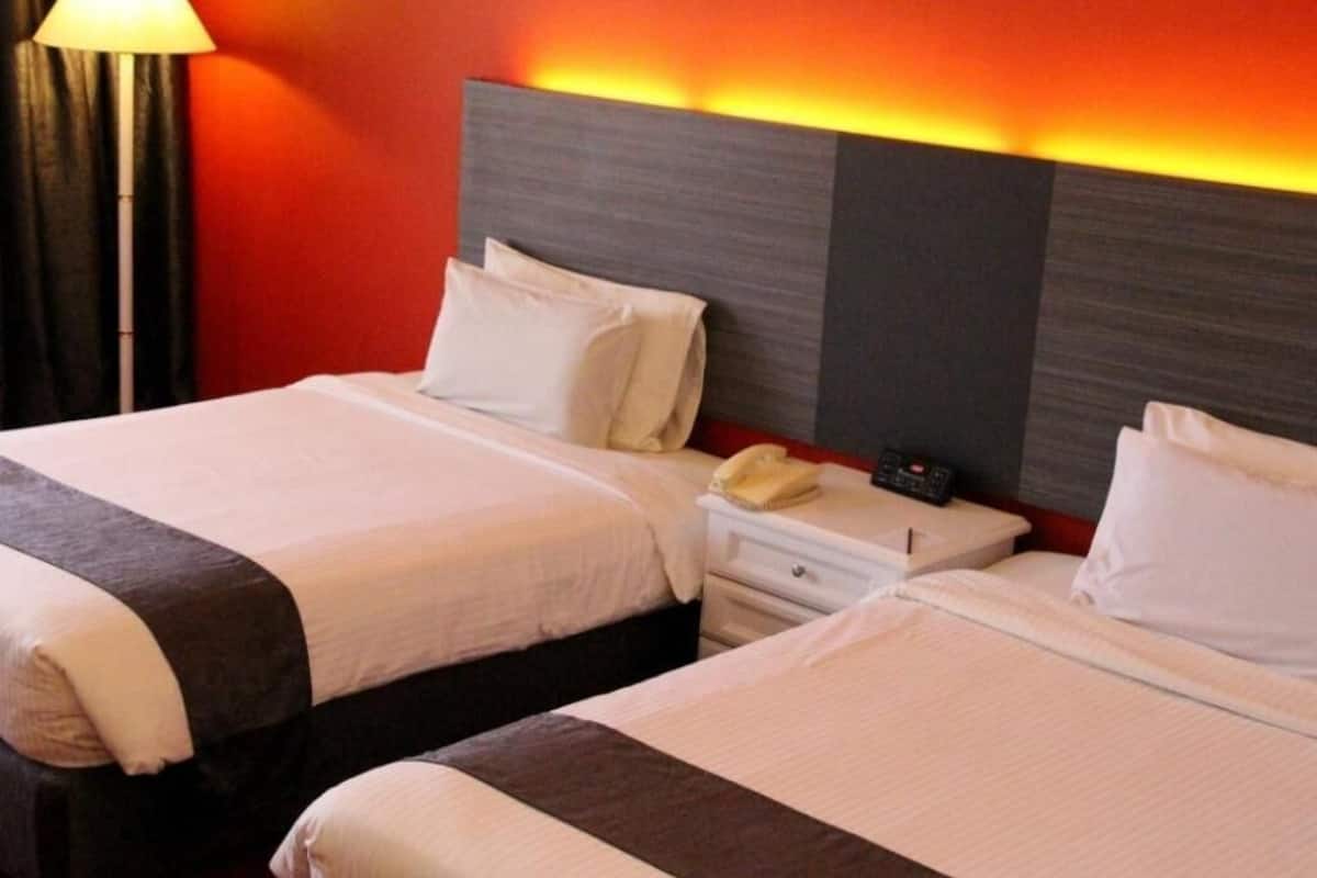 Zwei Betten mit weißer Bettwäsche, ein Nachttischtelefon und eine Lampe.