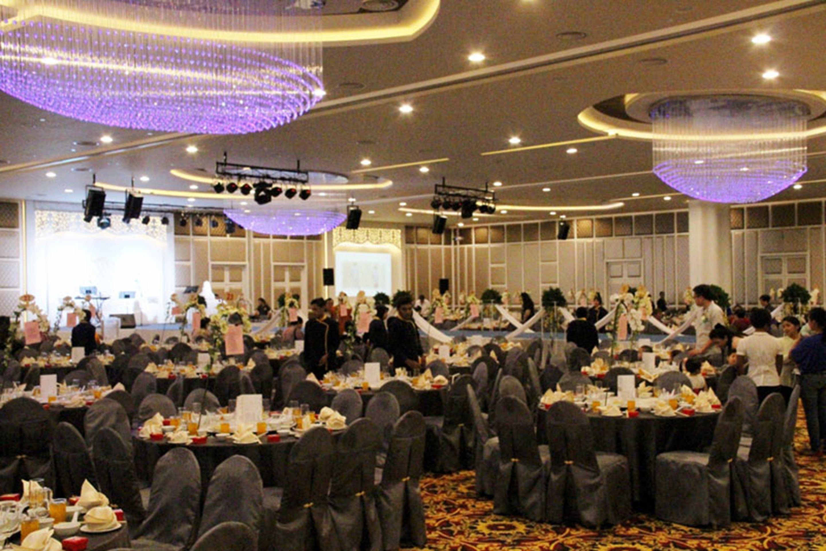 A banquet hall with round tables, gray chairs, and purple chandeliers.