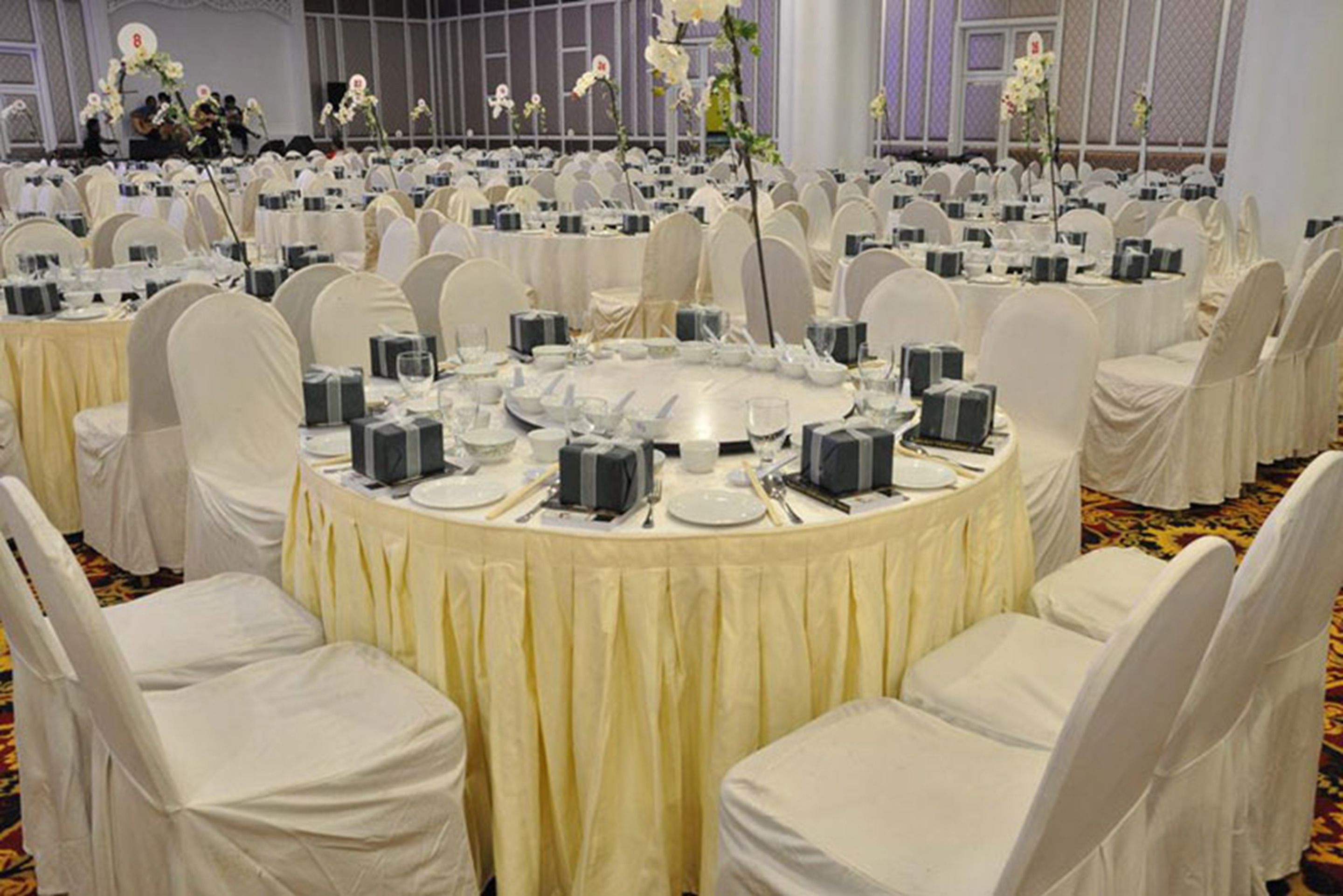 A banquet hall with round tables covered in white tablecloths, each surrounded by white chairs.