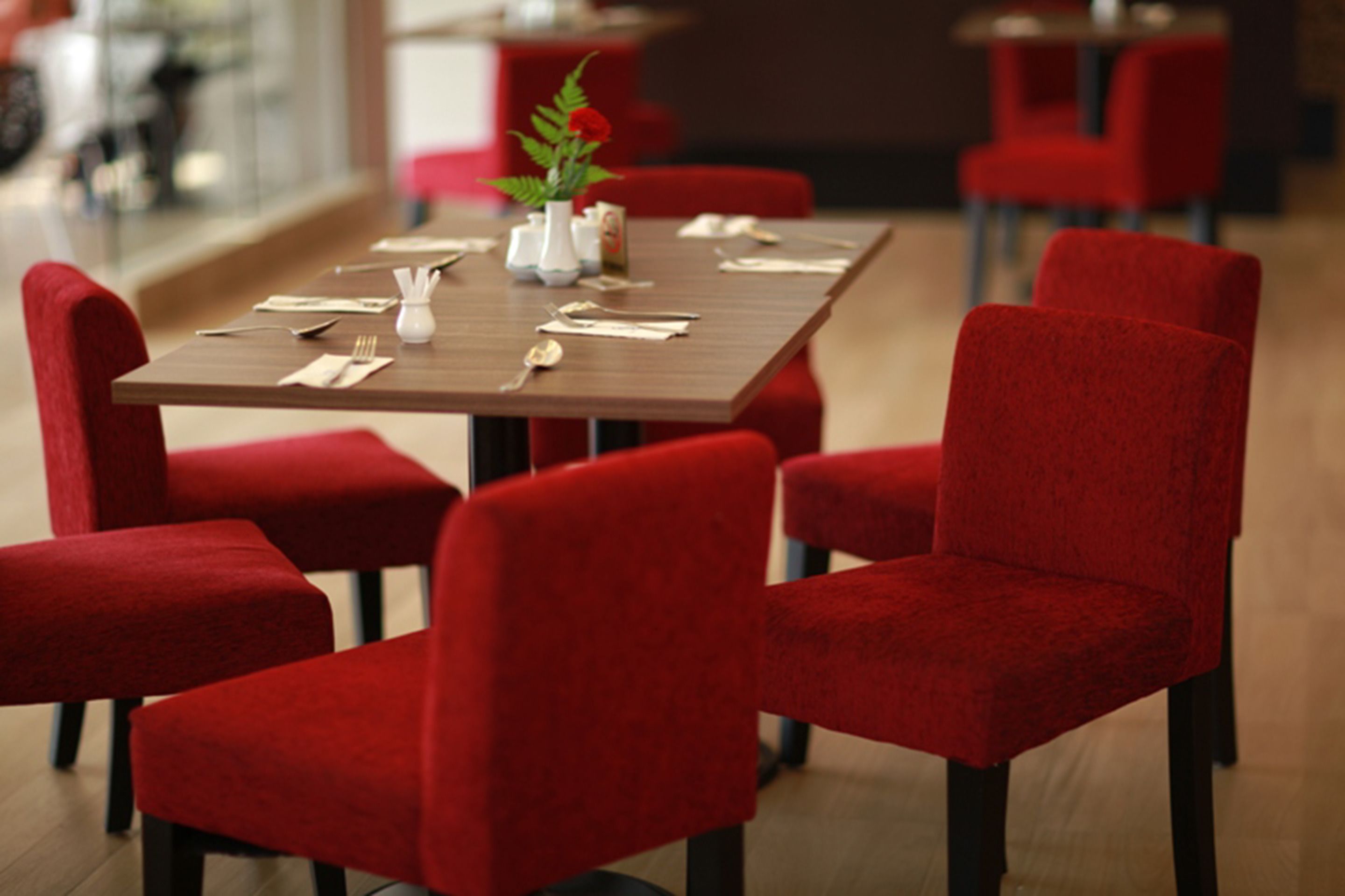 Un coin repas avec une table rectangulaire dressée pour quatre personnes, entourée de chaises à revêtement rouge.
