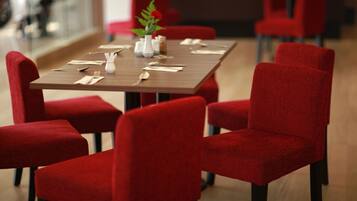 Un coin repas avec une table rectangulaire dressée pour quatre personnes, entourée de chaises à revêtement rouge.