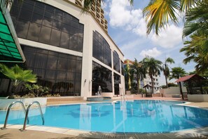 A swimming pool with a clear blue water, surrounded by palm trees and a modern building with large windows.