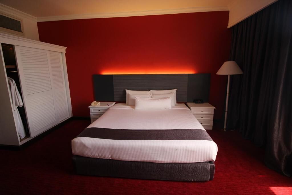 A hotel room with a large bed, a bedside table, a nightstand, a wardrobe, and a lamp.