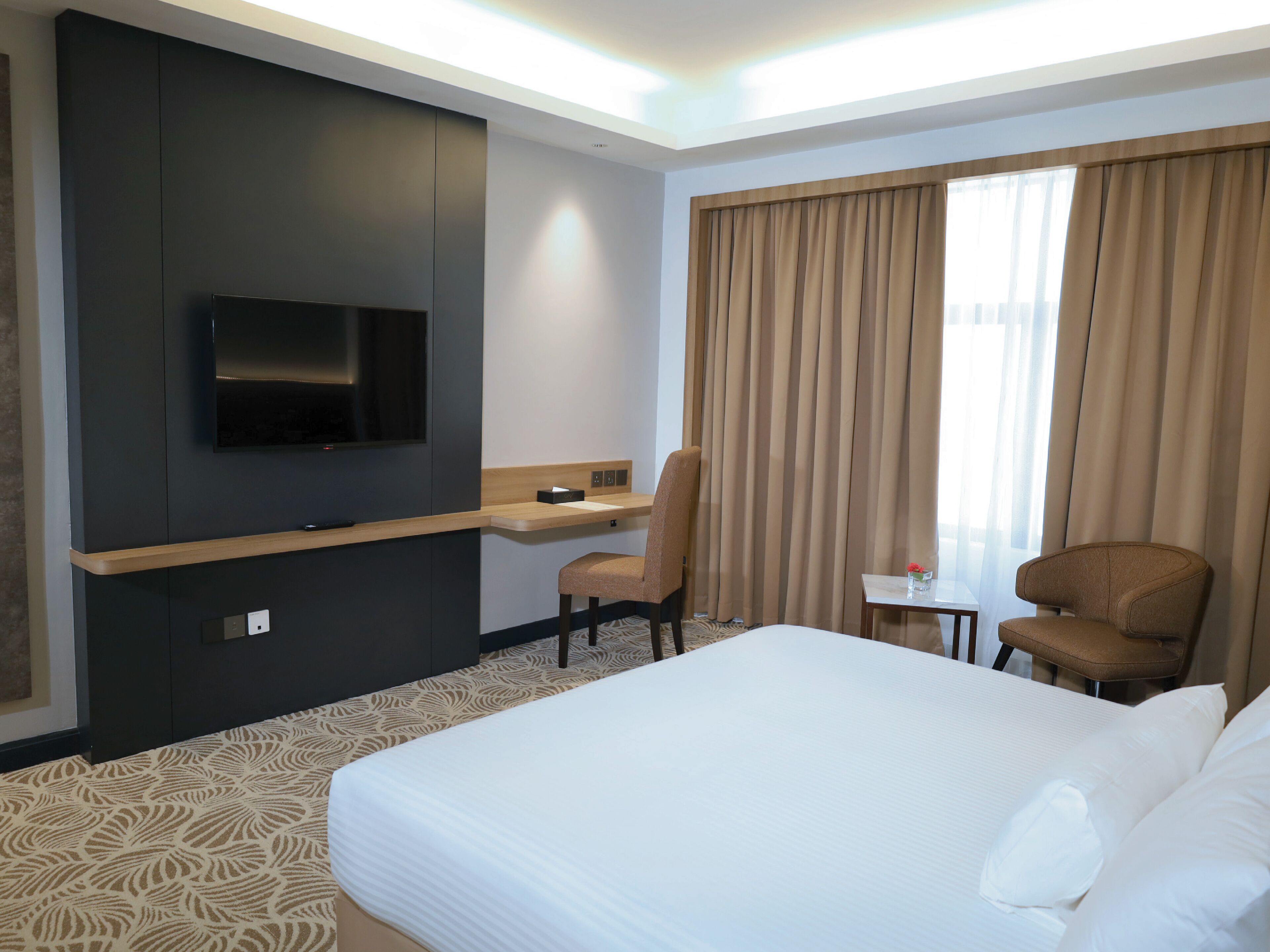 A hotel room with a bed, a desk, a chair, a television, and a window with curtains.