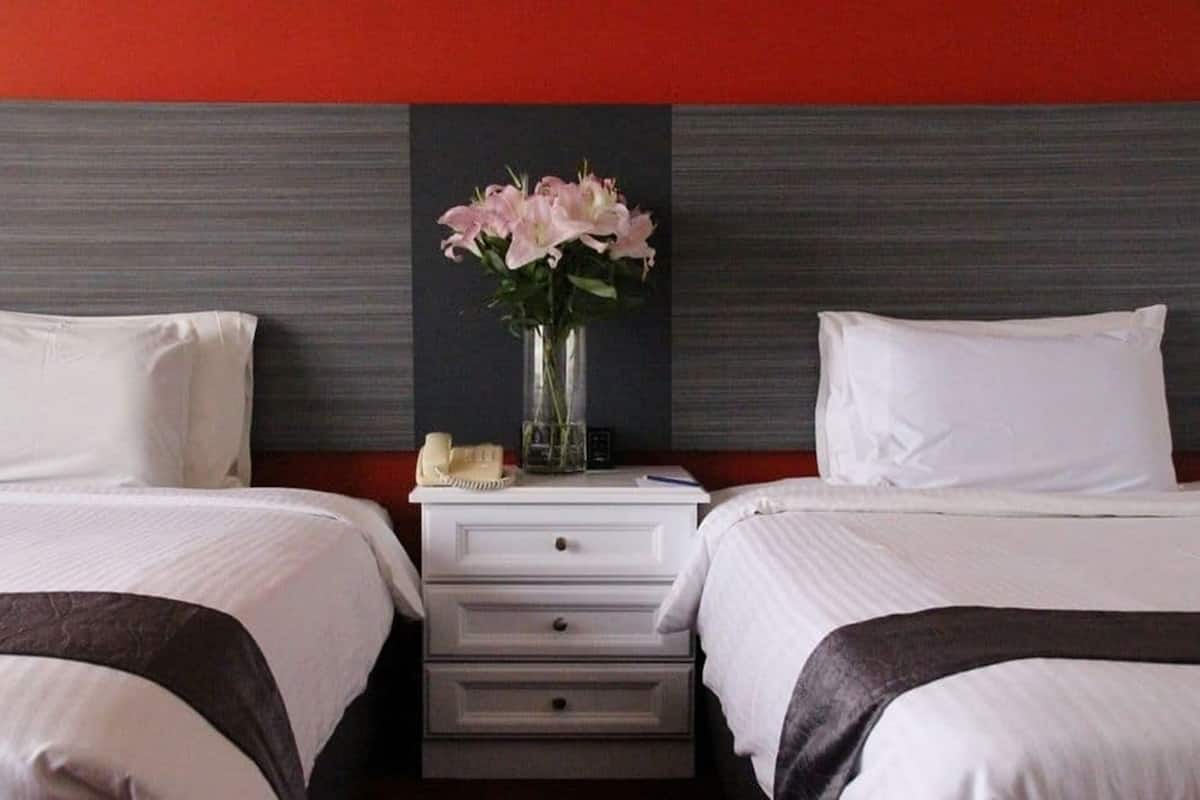 Ein Hotelzimmer mit zwei Betten, einem Nachttisch mit Blumenvase und einer roten Akzentwand.