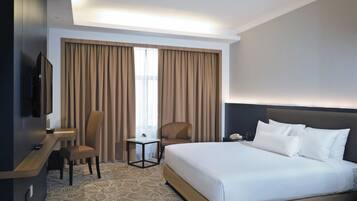 Habitación de hotel con una cama grande, un escritorio con una silla, un televisor y una ventana con cortinas.