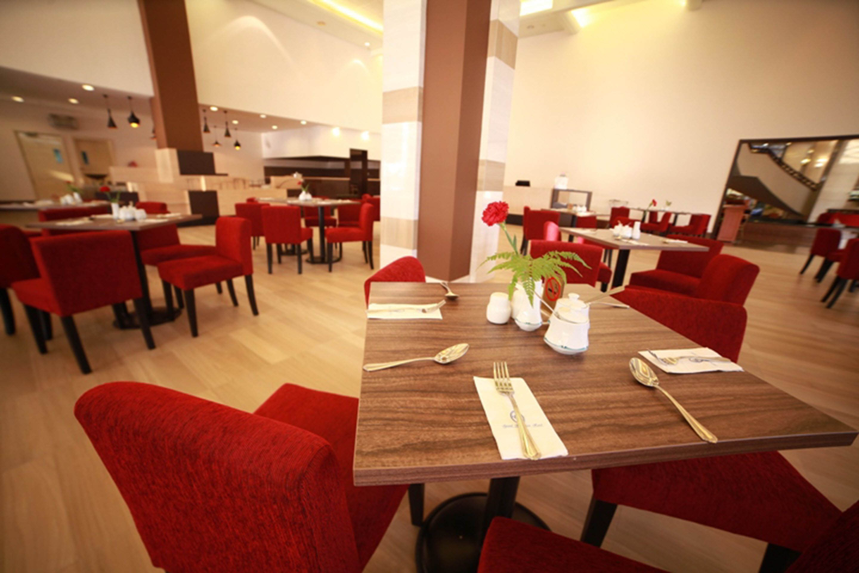Un espace repas moderne avec des chaises et des tables rouges, équipé de couverts et de sali ères et de poivrières.