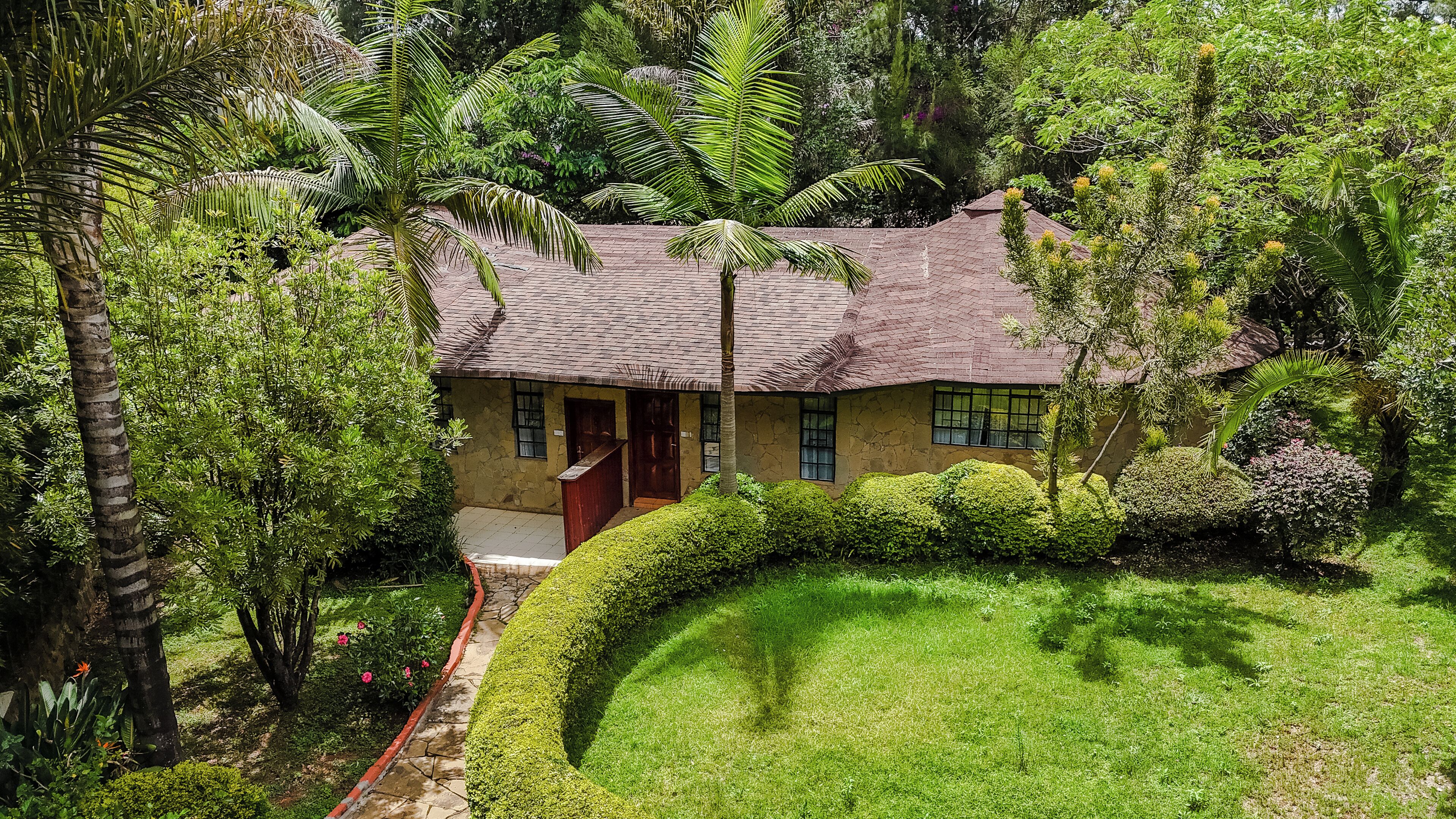 A traditional house with a tiled roof, surrounded by lush greenery and a well-maintained lawn.