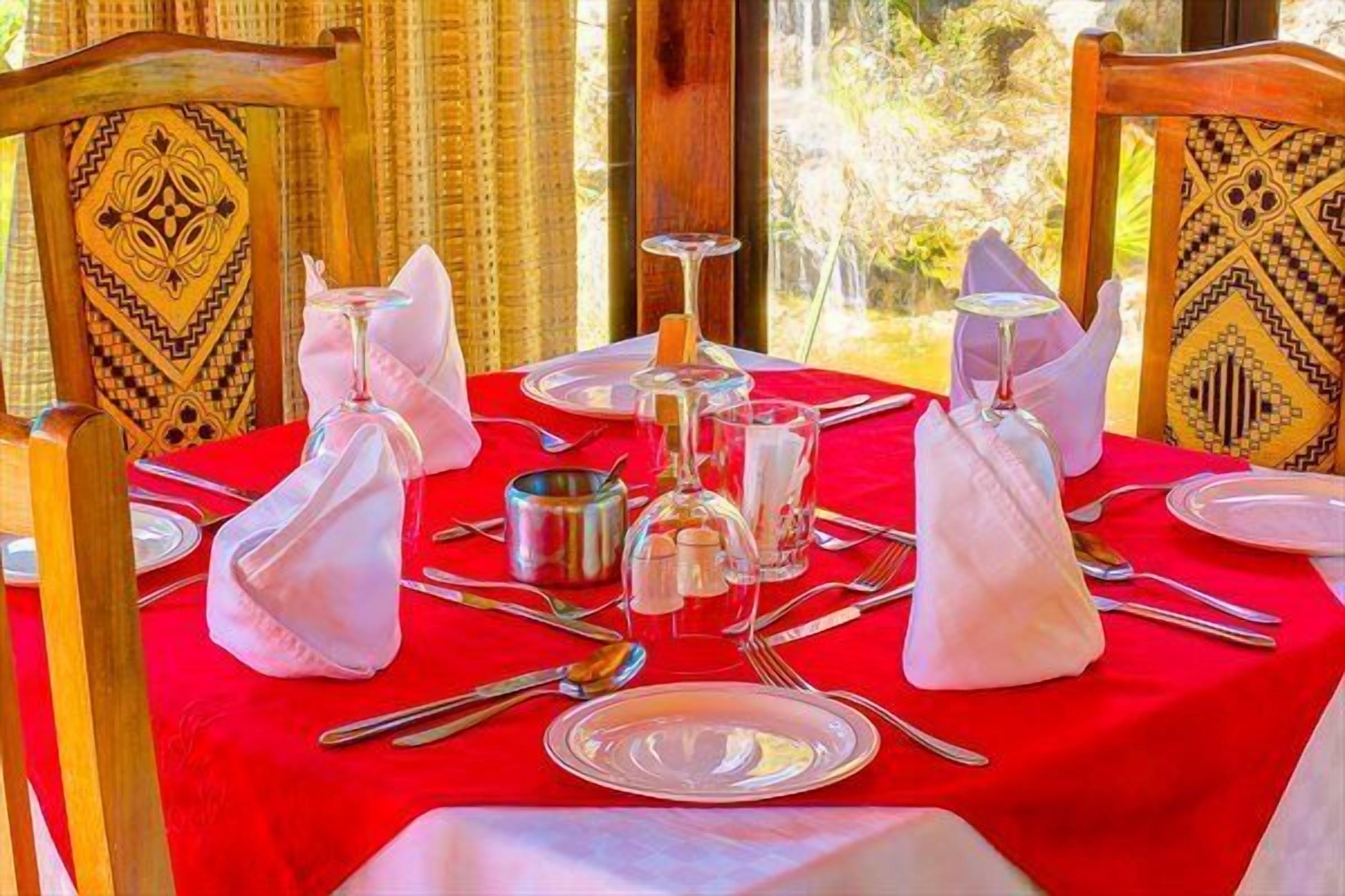 Una mesa dispuesta para comer, con mantel rojo, servilletas blancas y cubiertos.