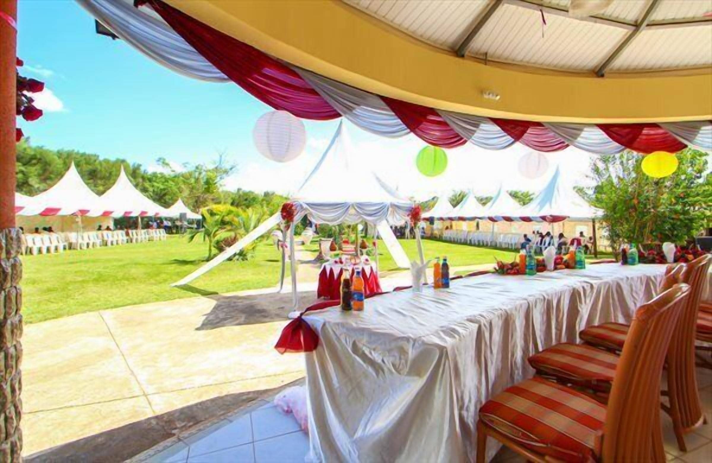 An outdoor event space with a covered area, tables with chairs, and tents in the background.