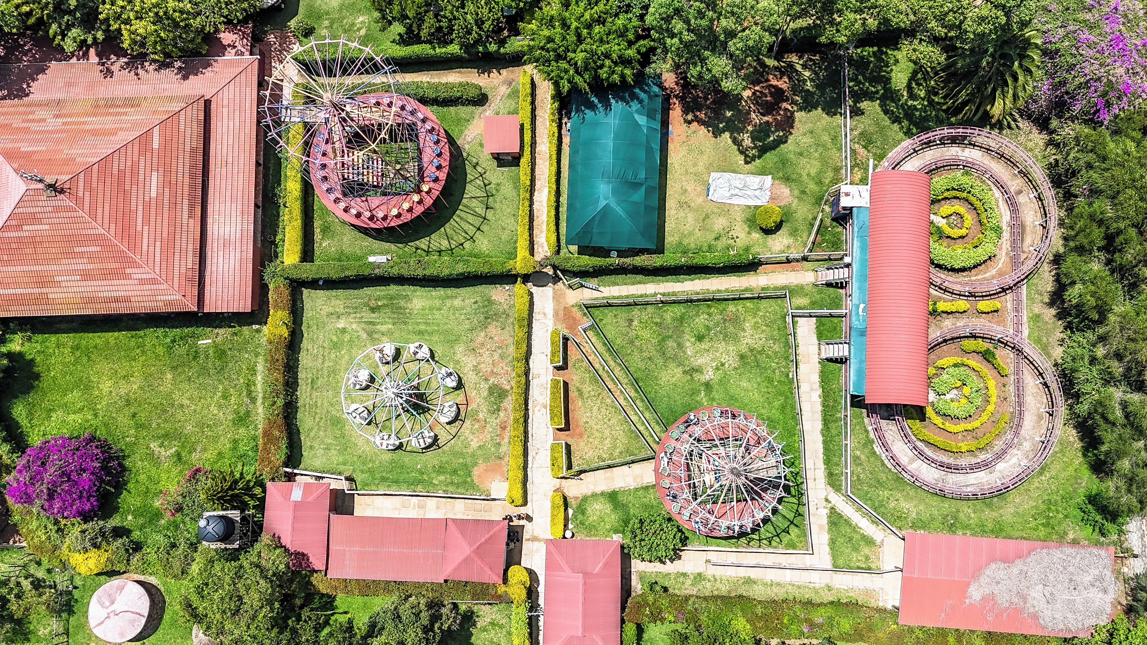 An aerial view of a park with a Ferris wheel, a carousel, and a circular garden with a red roof.